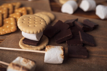 marshmallows, chocolate and cookies for making smore on brown background. view from above. copy space