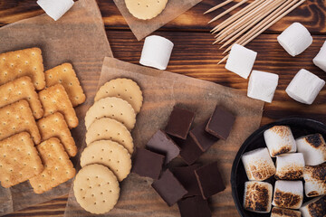 marshmallows, chocolate and cookies for making smore on brown background. view from above. copy...