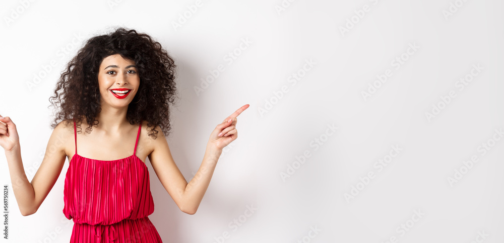 Wall mural happy lady with curly hairstyle and red lips, smiling white teeth, pointing sideways at two ways, sh