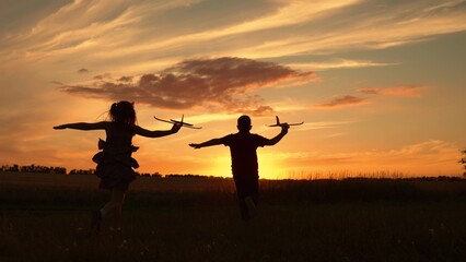 Children aviators boy girl run with toy plane across field in rays of sunset. Child wants to become...