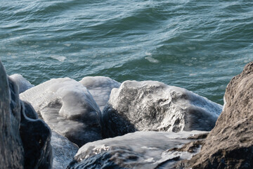 Frozen icy rocks in front of cold winter blue lake.