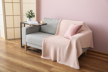 Fototapeta na wymiar Table with houseplant, cup, book and grey sofa near pink wall