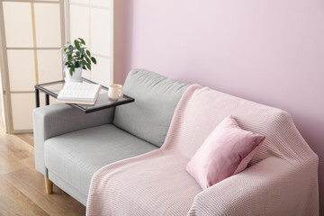 Table with houseplant, cup, book and grey sofa near pink wall