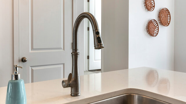 Panorama Stainless steel sink with deck mounted one-handle faucet. Sink and liquid soap bottle on the kitchen island with white marble top against the white interior walls and door.