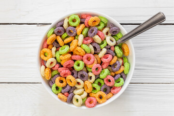 Colored breakfast cereals laid out in a bowl on a white wooden background, top view, children's...