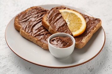 Plate of tasty toasts with hazelnut butter and orange slice on light background, closeup