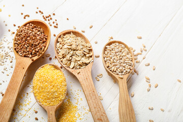 Spoons with different cereals on light wooden background, closeup