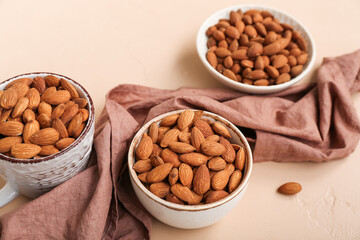 Bowls and cup with almond nuts on color background