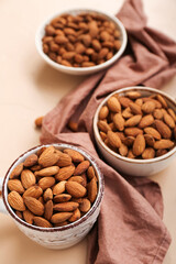Bowls and cup with almond nuts on color background, closeup