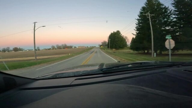 Point of View - driving on a rural county road through a small town and approaching a strop sign; in American Midwest at sunrise in late Autumn or early spring