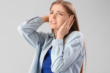 Young woman suffering from loud noise on grey background, closeup