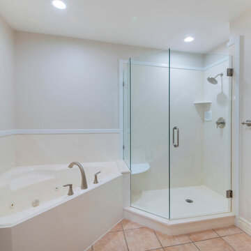 Square Bathroom interior with corner shower stall and bathtub. There is a toilet near the frameless shower stall with wall mounted shower head, shelf and seat beside the tub with deck mounted faucet.
