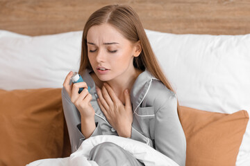 Sick young woman with inhaler in bed