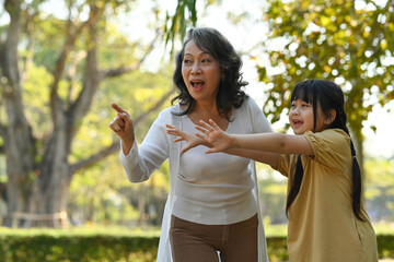 Joyful little asian child having fun while walking in public park with grandmother. Loving family relationship concept
