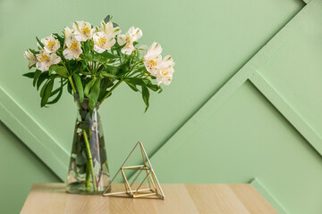 Vase with bouquet of alstroemeria flowers on wooden table near green wall