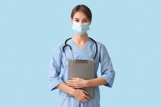 Female Medical Intern In Mask With Clipboard On Blue Background