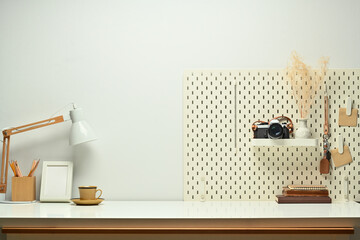 Stylish workplace with books, camera, lamp and peg board on wooden table against. Copy space for your text