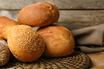 Wicker mat with loaves of different bread on wooden background