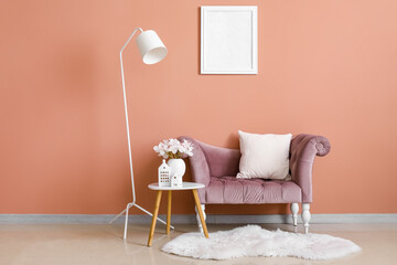 House candle holders, vase with orchid flowers on table and armchair near orange wall