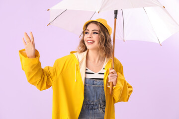 Stylish young woman in autumn clothes and with umbrella on lilac background