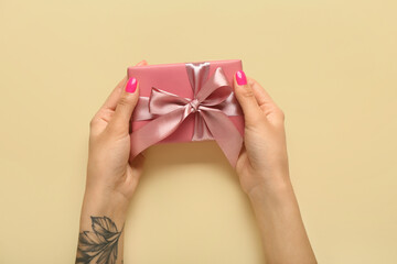 Female hands holding pink gift box on yellow background. Hello spring