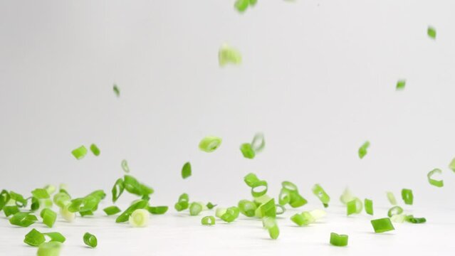 Diced and chopped green onion pieces falling and bouncing onto white table top in slow motion