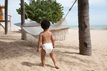 Cute boy toddler on summer vacation at the beach. He has brown curly hair and is wearing a diaper....