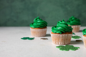 Tasty cupcakes for St. Patrick's Day and clovers on white table against green background