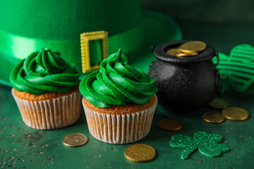 Tasty cupcakes for St. Patrick's Day, leprechaun hat and pot of coins on green background