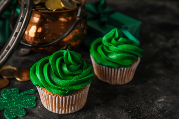 Tasty cupcakes for St. Patrick's Day, pot of coins and horseshoe on black grunge table