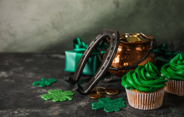 Tasty cupcakes for St. Patrick's Day, pot of coins and horseshoe on black grunge table