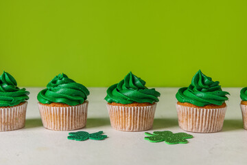 Obraz na płótnie Canvas Tasty cupcakes for St. Patrick's Day and clovers on white table against green background