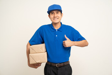 Happy delivery asian man in blue uniform standing holding box parcel cardboard on isolated white...