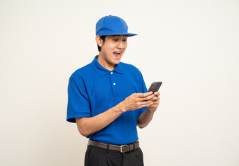 Asian man in blue uniform standing holding smartphone on isolated white background. Male service worker with cell phone. Delivery courier shipping service