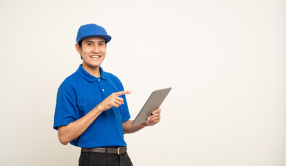 Asian man in blue uniform standing holding digital tablet computer on isolated white background. Male service worker with cell phone. Delivery courier shipping service