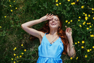 A woman in spring lies on the green grass with yellow flowers smile with teeth happiness in a blue...