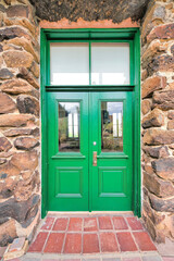 Obraz na płótnie Canvas Tucson, Arizona- Large green front door with window panel and transom window. Double door with large transom window in between the rockwalls.