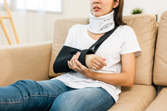 Happy woman recovery from accident fracture broken bone injury with leg splints in cast neck splints collar arm splints sling support arm in living room. Social security and health insurance concept.