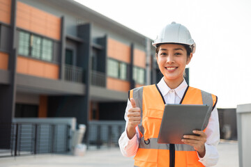 Confident asian engineer woman Using tablet for checking and maintenance to inspection at modern home building construction. Architect working with white safety helmet in construction site