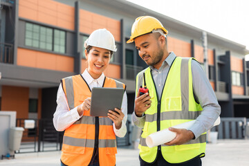 Two Asian worker engineer architect man and woman architect looking construction with white safety helmet in modern home building construction. Work planning with blueprint and tablet.