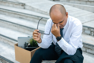 Sadness depressed Businessman with box cardboard packing personal items after losing jobs. Failure businessman sitting at stair front of building. Your fired Unemployed Jobless People Crisis