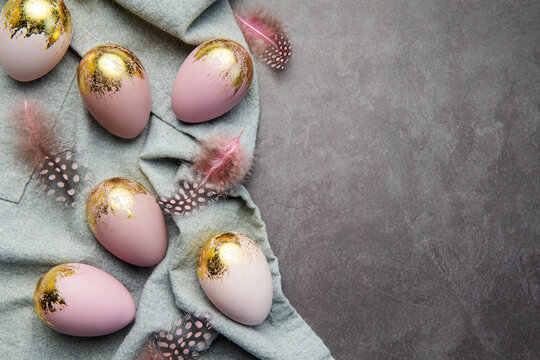 Easter eggs are painted with violet and gold paint on a gray linen background.