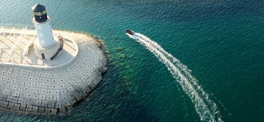 Amazing aerial drone view of lighthouse, dam and motor boat on Lustica bay near Tivat, Montenegro on sunny day. Picturesque view of light house in the sea - obrazy, fototapety, plakaty