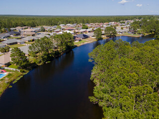 River running amid residential neighborhood in Navarre Florida on a sunny day. Aerial view of scenic residences and houses surrounded by lush green trees landscape.