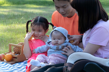 Obraz premium Cheerful Asian family having a good time on picnic holiday together, happy mother, father and two daughters at summer park