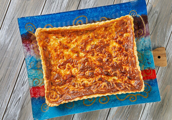 Tart with potatoes and cheese on glass plate on wooden background
