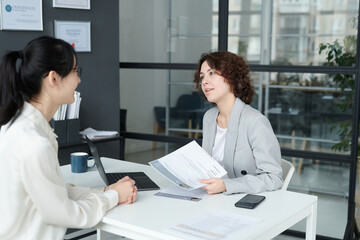 Young businesswoman examining resume and asking questions to employee during business meeting