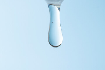 Hyaluronic acid flowing in a jet on a blue background close-up. Cosmetic transparent liquid product...