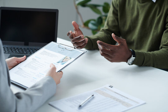 Close-up of young woman interviewing man at table during job interview, she reading resume and asking questions