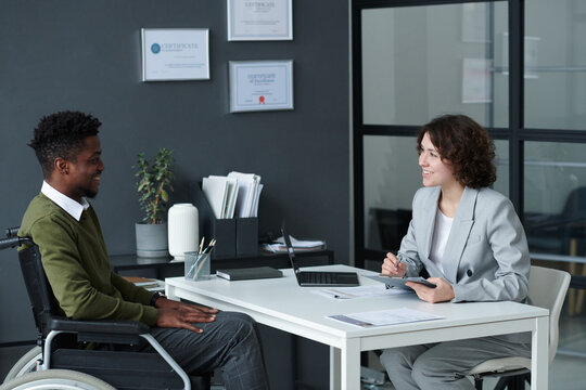 Young businesswoman interviewing candidate with disability while they sitting at table during job interview